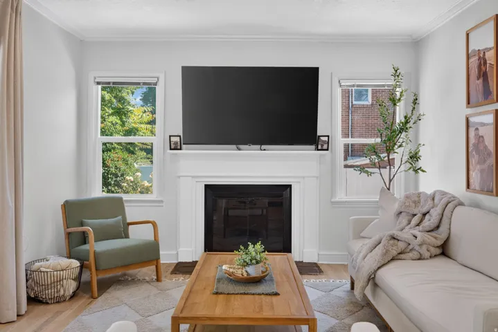 Living area featuring a fireplace with a white mantel, crown molding, and light wood-finish flooring