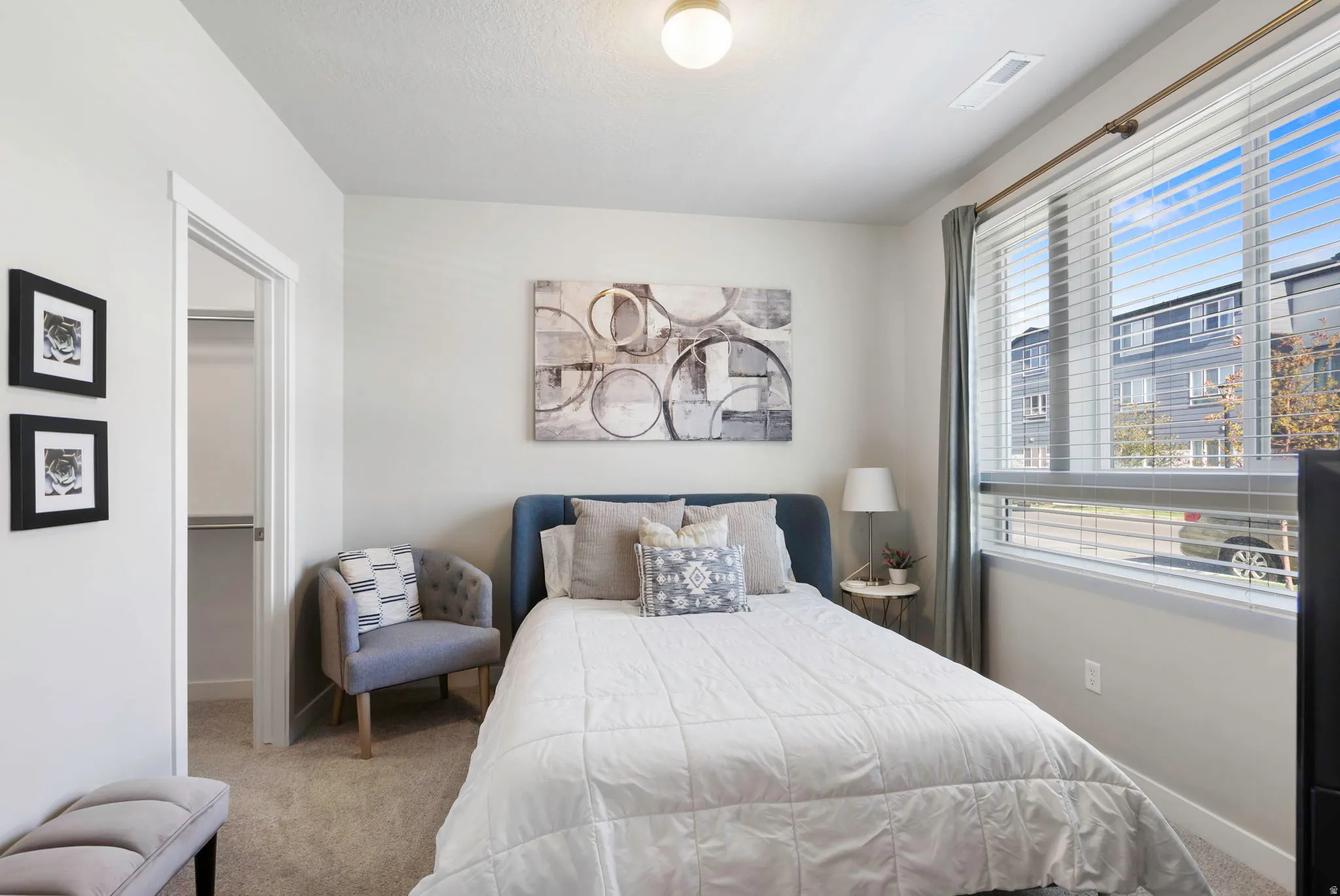 Light-filled interior featuring a large window with horizontal blinds, neutral wall tones, and carpet flooring