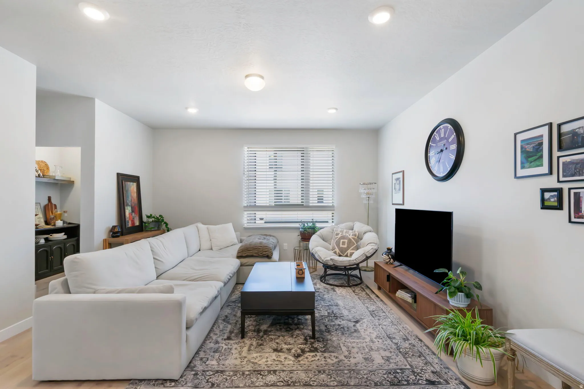 Spacious living area featuring light wood-finish flooring, recessed lighting, and a large window with blinds