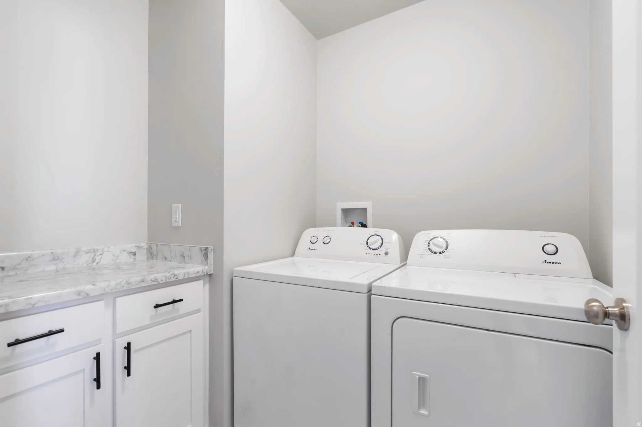 Laundry area with white cabinetry, matte black hardware, and a stone-finish countertop