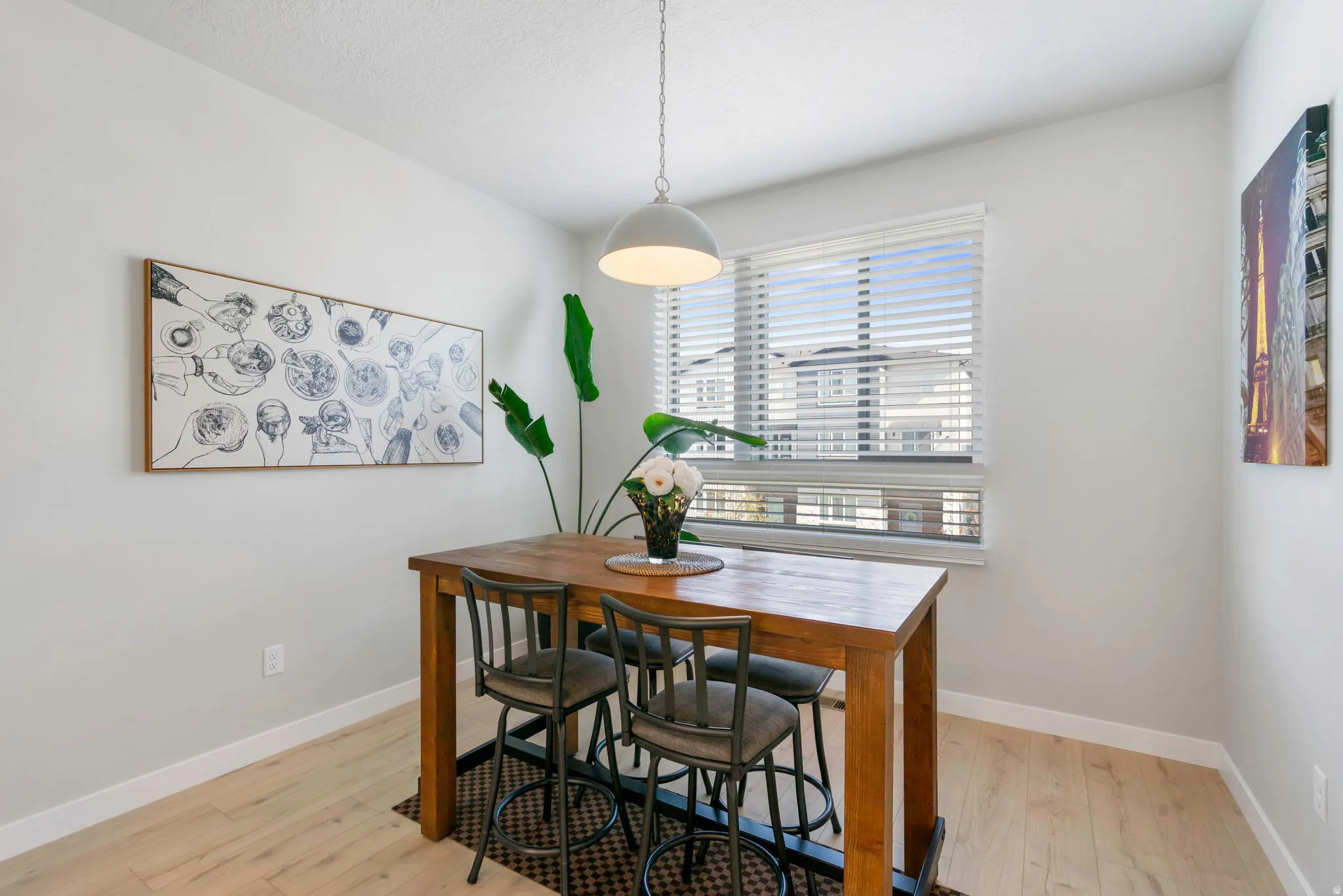 Dining area featuring wood-finish flooring, a contemporary pendant light fixture, and a large window with horizontal blinds