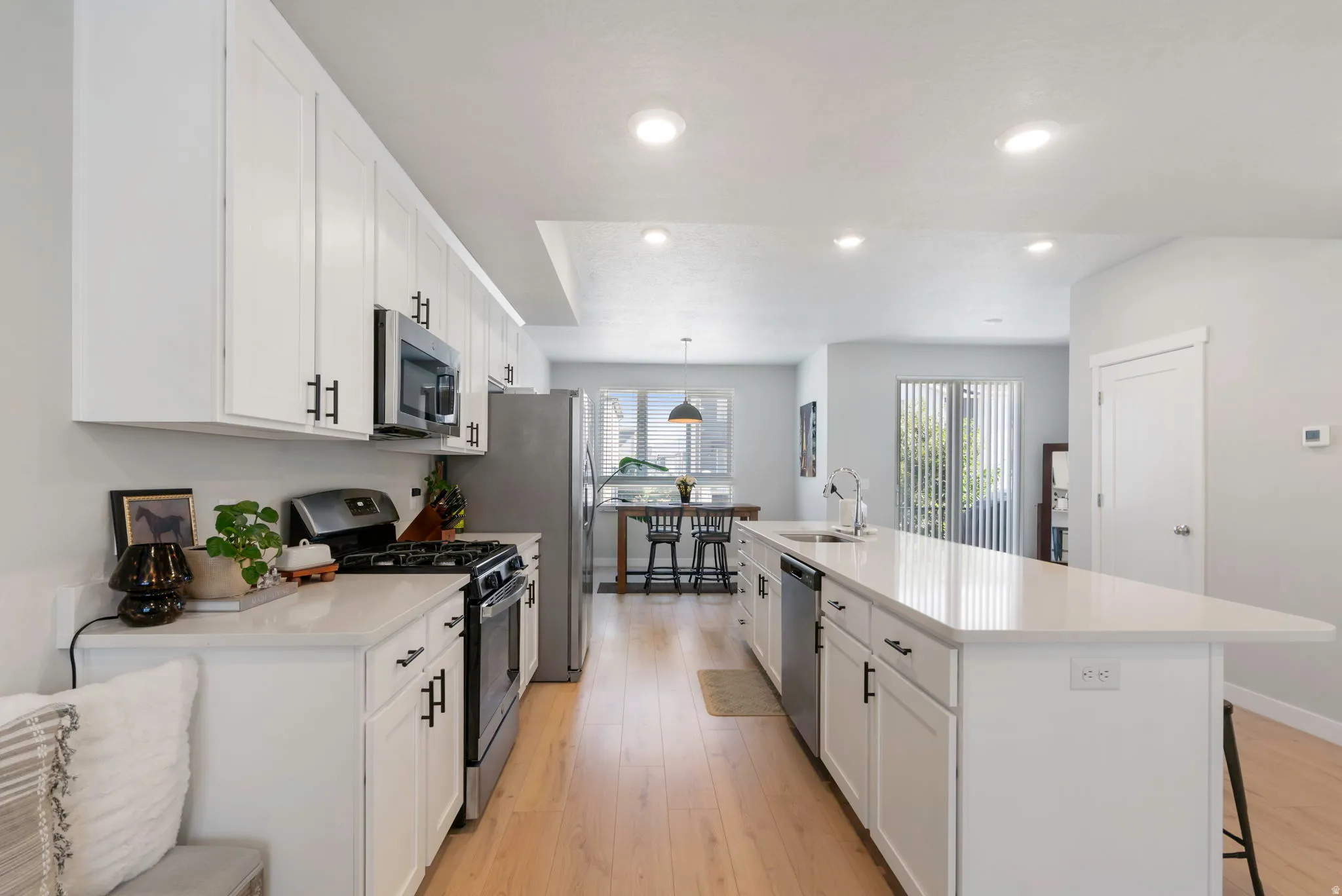 Contemporary kitchen featuring white cabinetry, stainless steel appliances, light wood-finish flooring, recessed lighting, and an expansive island with a sink