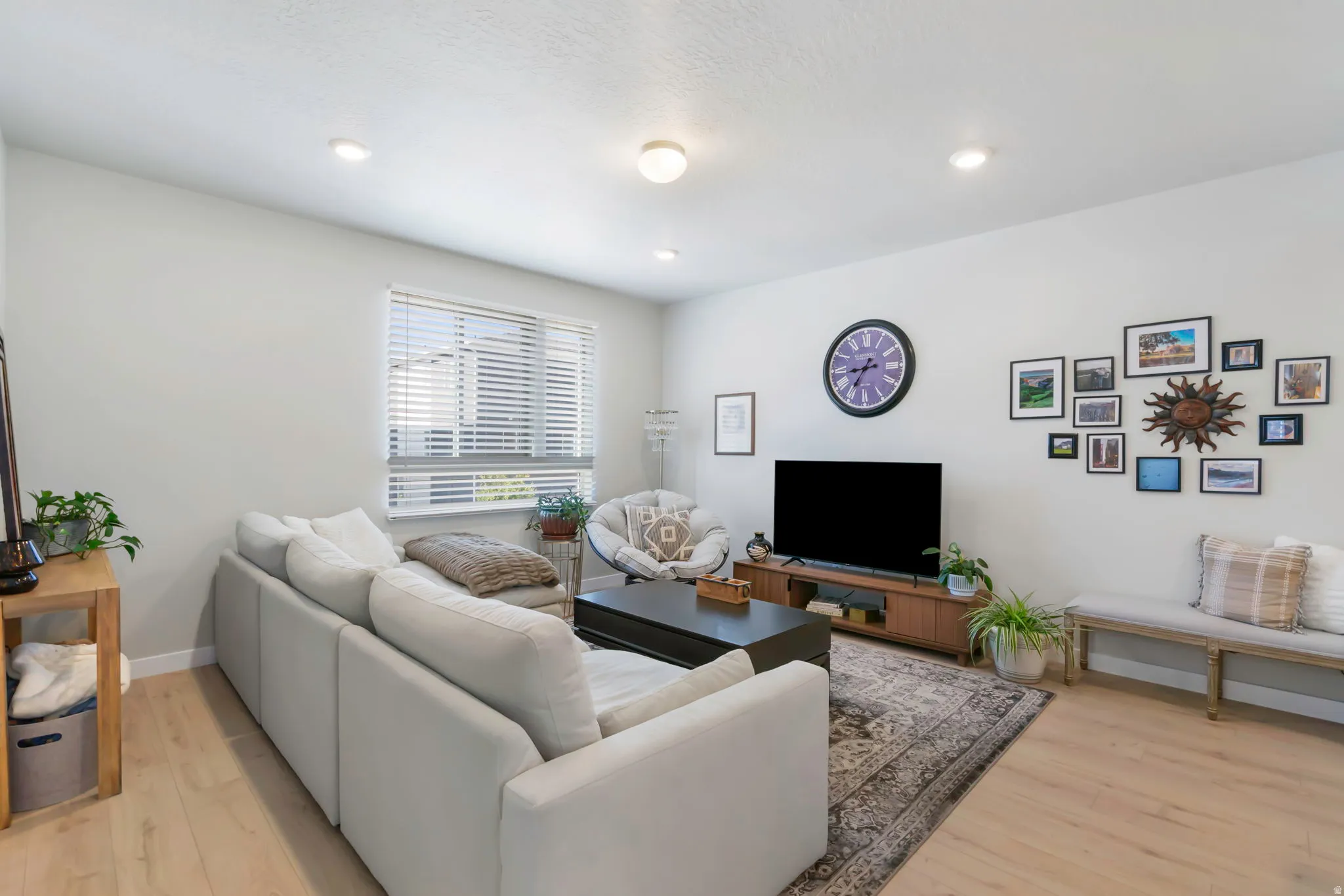 Spacious living area featuring light wood-finish flooring, recessed lighting, and a large window with blinds