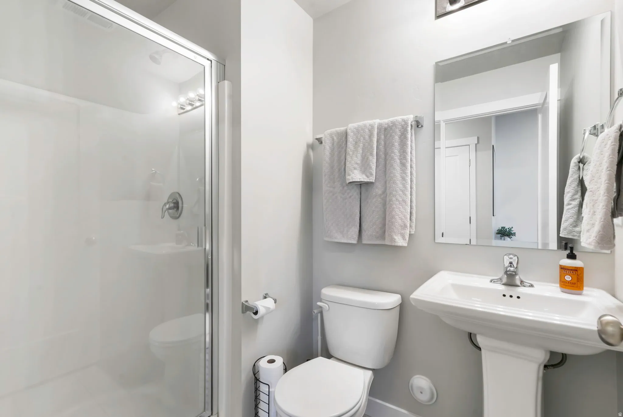Bathroom featuring a glass-enclosed shower, pedestal sink, wall-mounted mirror, and chrome fixtures