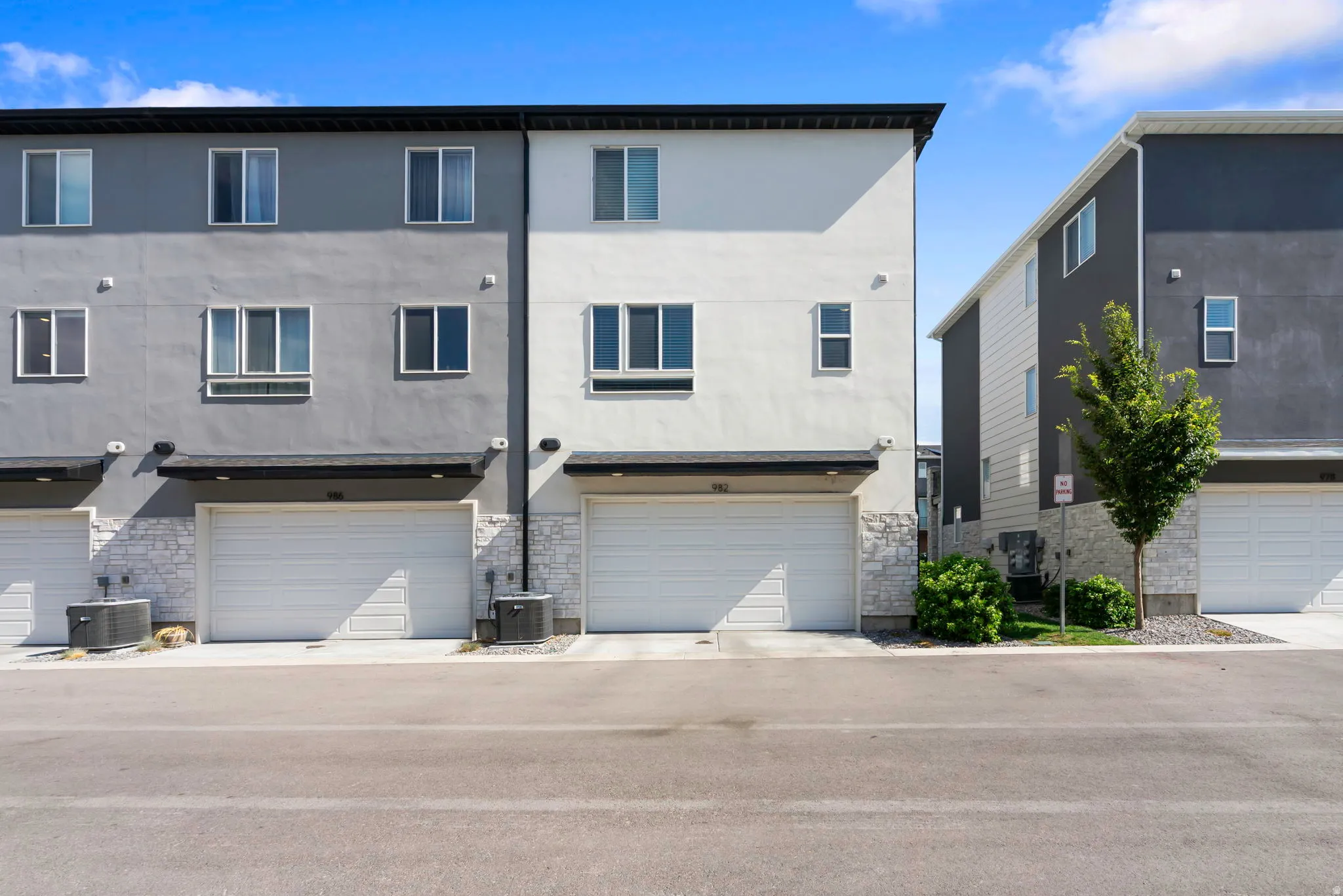 Contemporary townhome facade featuring a two-tone exterior, an integrated garage, stone veneer accents, and multiple window placements