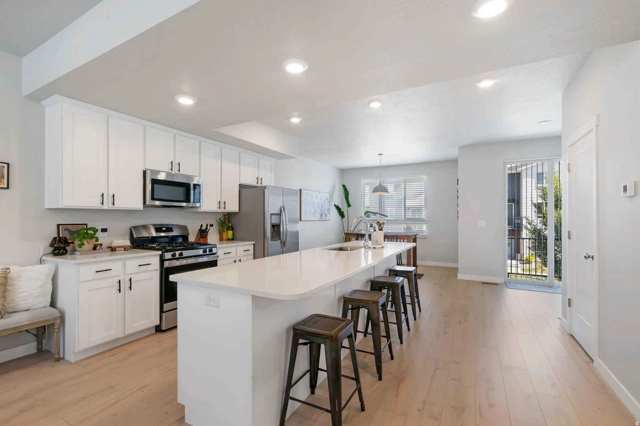 Open-concept kitchen featuring white cabinetry, stainless steel appliances, a gas range, a large center island with seating, and wood-finish flooring