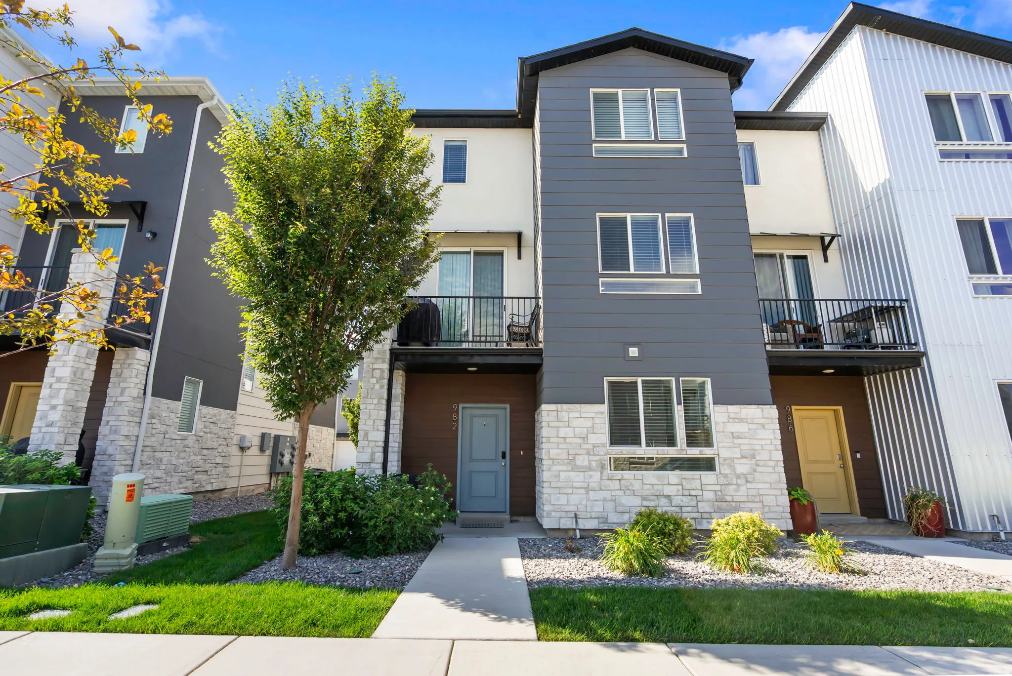 Modern three-story townhouse featuring a multi-textured facade with horizontal siding, stone veneer, and smooth stucco