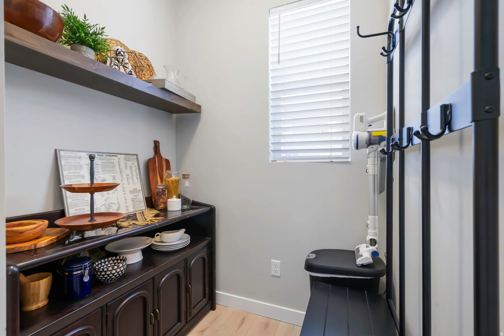 Integrated storage area with hardwood-style flooring, a dark wood-finish cabinet with arched doors, and an open floating shelf