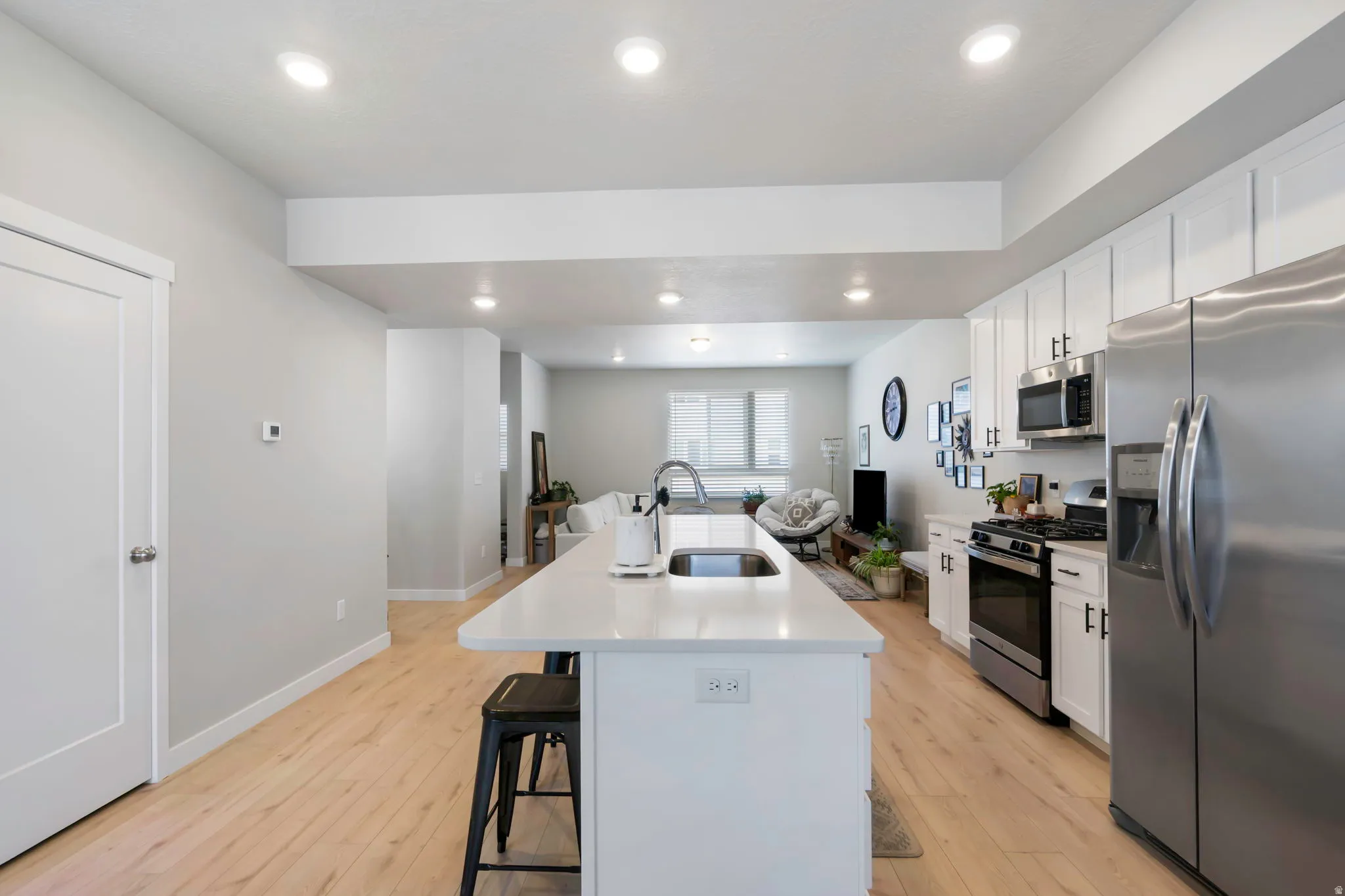 Contemporary kitchen featuring a large central island with an undermount sink, white cabinetry, stainless steel appliances, and wood-finish flooring
