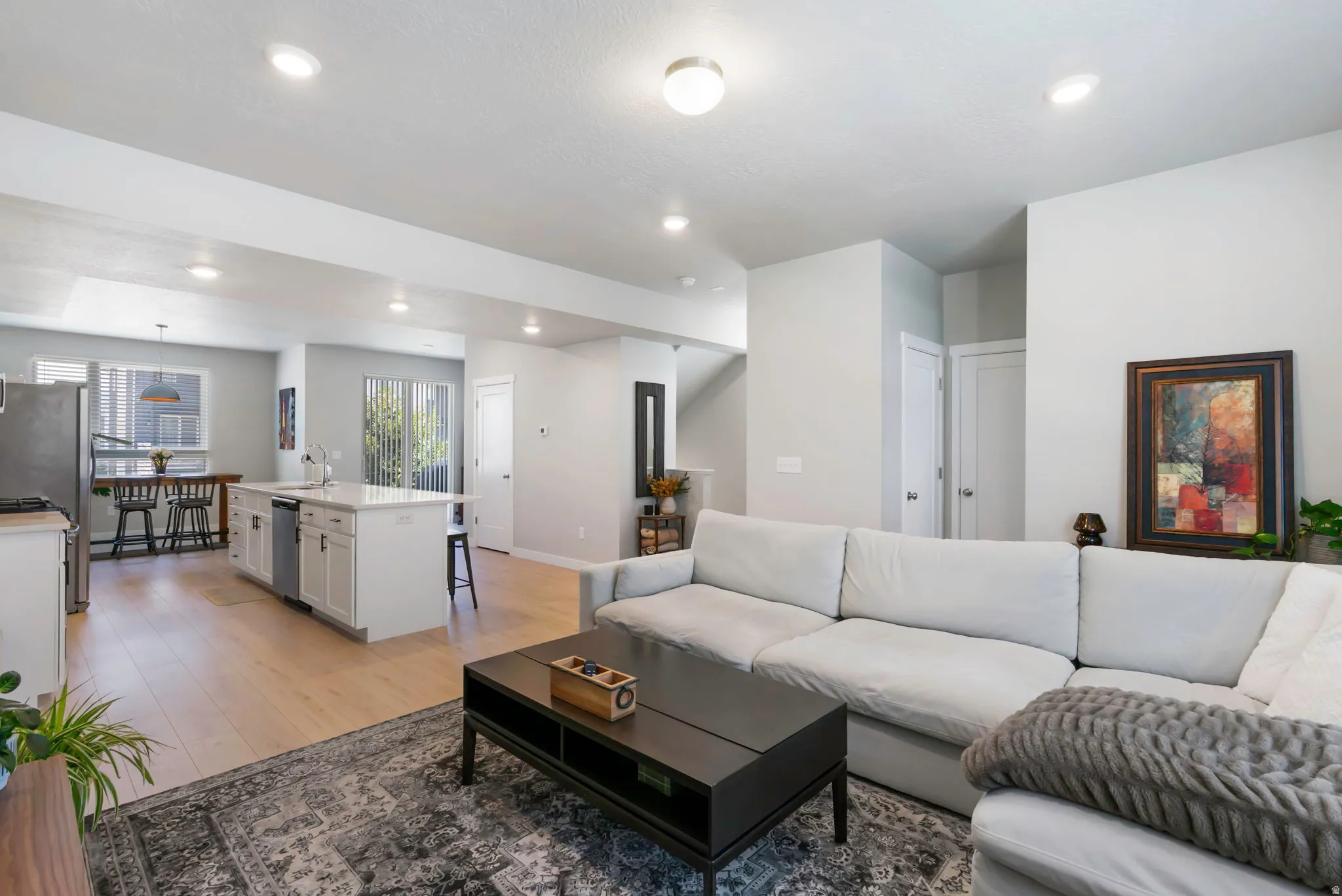 Open-concept living area featuring light wood-finish flooring, recessed lighting, a white kitchen island with an undermount sink, a stainless steel dishwasher, and sliding glass doors