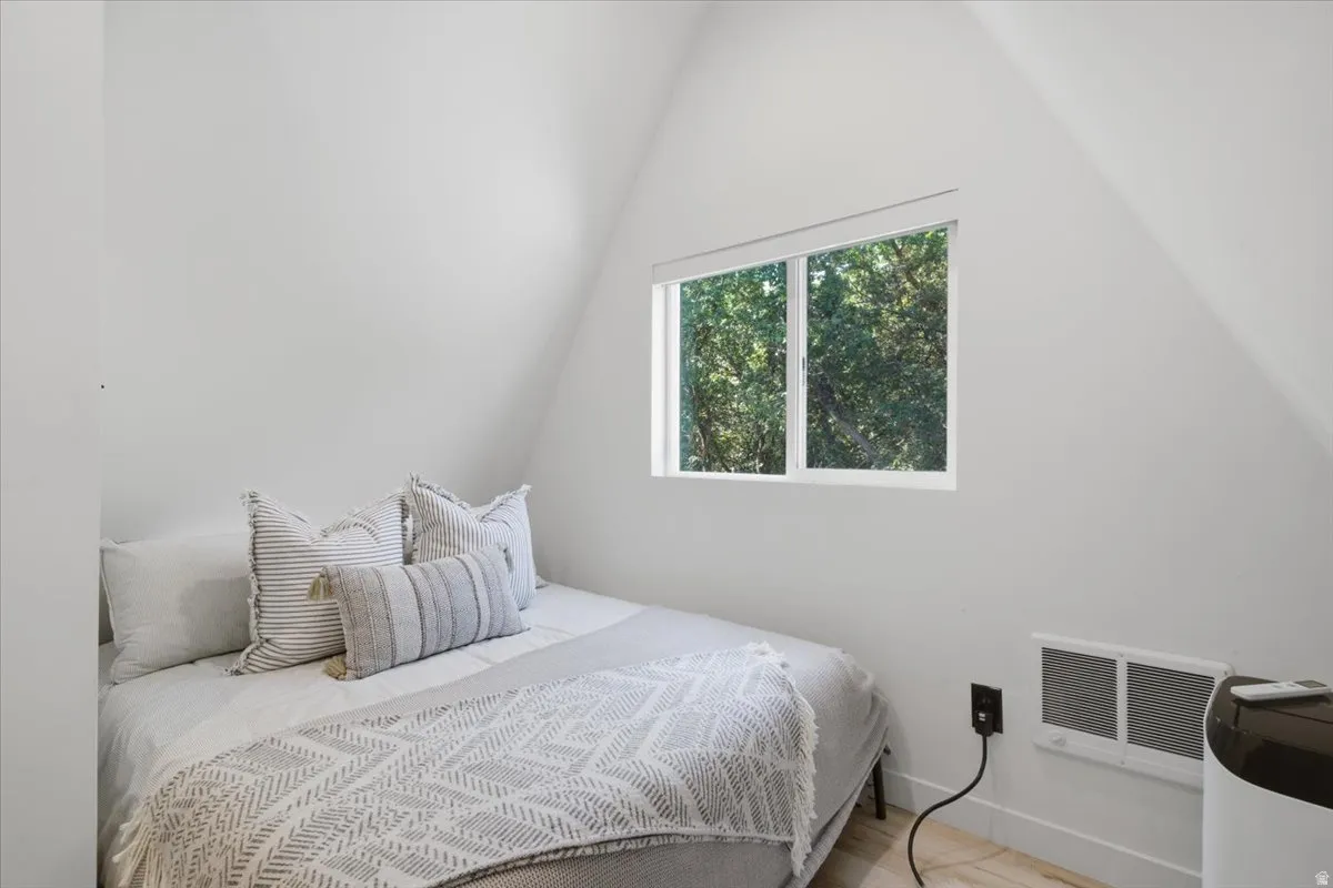 Angled ceiling room with a double-pane window, white wall finishes, and light wood-finish flooring