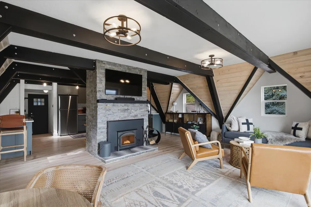 Vaulted ceiling living area featuring exposed black beams and light wood-finish accent walls