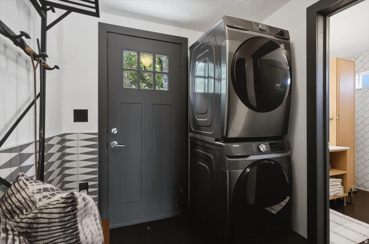 Modern utility space featuring a stacked washer and dryer, a dark paneled door with windowpanes, and geometric wall tiling