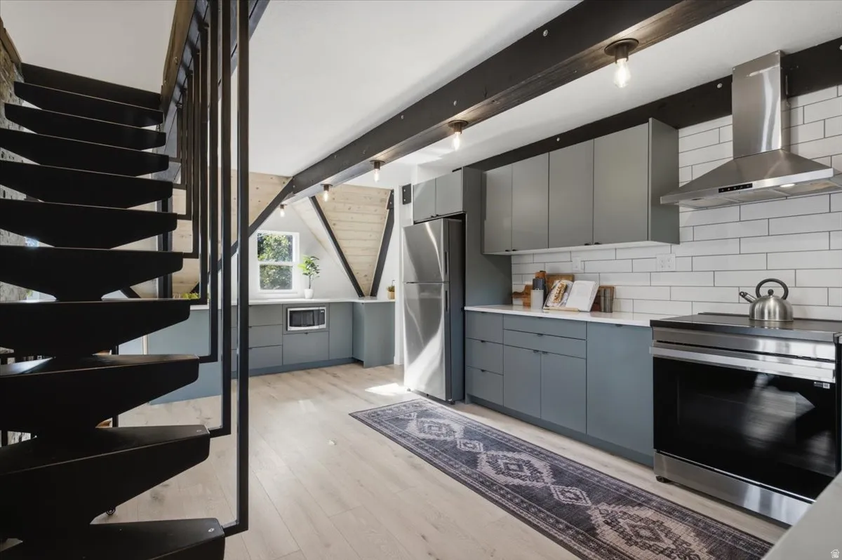 Kitchen featuring a black metal staircase, light wood-finish flooring, gray cabinetry, stainless steel appliances, and white subway tile backsplash
