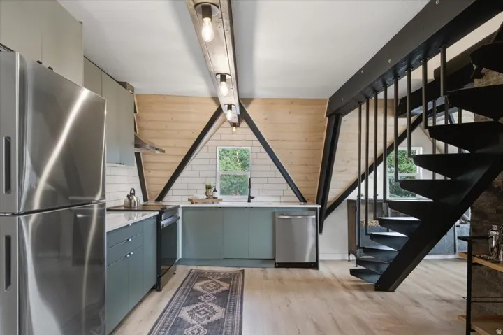 Kitchen featuring stainless steel appliances, light wood-finish flooring, light gray cabinetry, white subway tile backsplash, and a window with exterior foliage