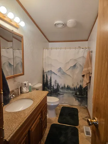 Bathroom featuring a granite-look countertop, wood-finish vanity cabinetry, built-in sink, and ceramic tile flooring
