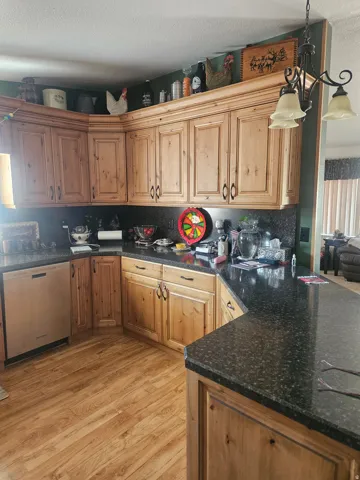 Kitchen featuring wood-finish flooring, dark speckled countertops, light wood cabinetry, and an integrated dishwasher