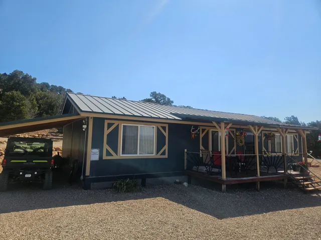 Dark-toned siding exterior with light wood-finish trim accents, a full-width covered porch with decorative railing, and a metal roof