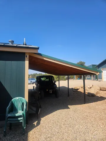 Carport structure with a green metal roof, wood-finish ceiling, and dark support pillars