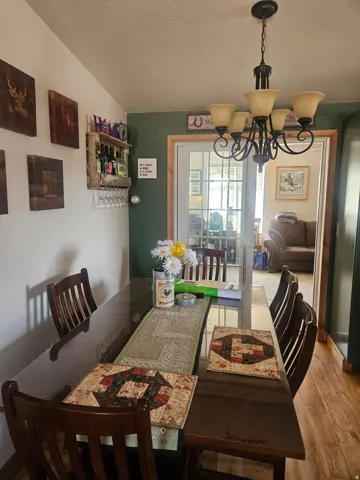 Dining area featuring wood-finish flooring, a six-light chandelier, a decorative wall-mounted wine rack, and a glass-top dining table
