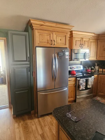 Kitchen featuring wood-finish cabinetry with crown molding, dark granite-style countertops, wood-finish flooring, a stainless steel refrigerator, and a stainless steel range with overhead microwave