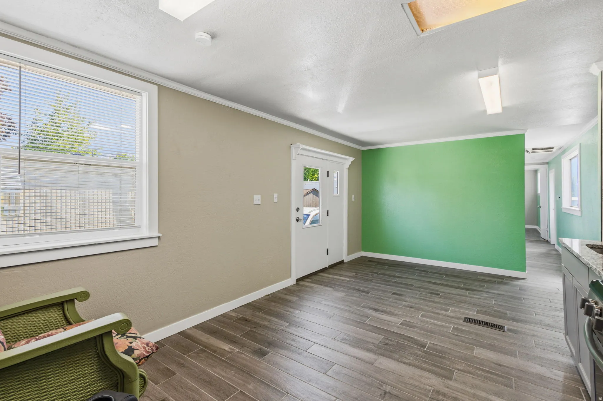 Spacious room featuring wood-finish flooring, a contemporary accent wall, and a large window with blinds