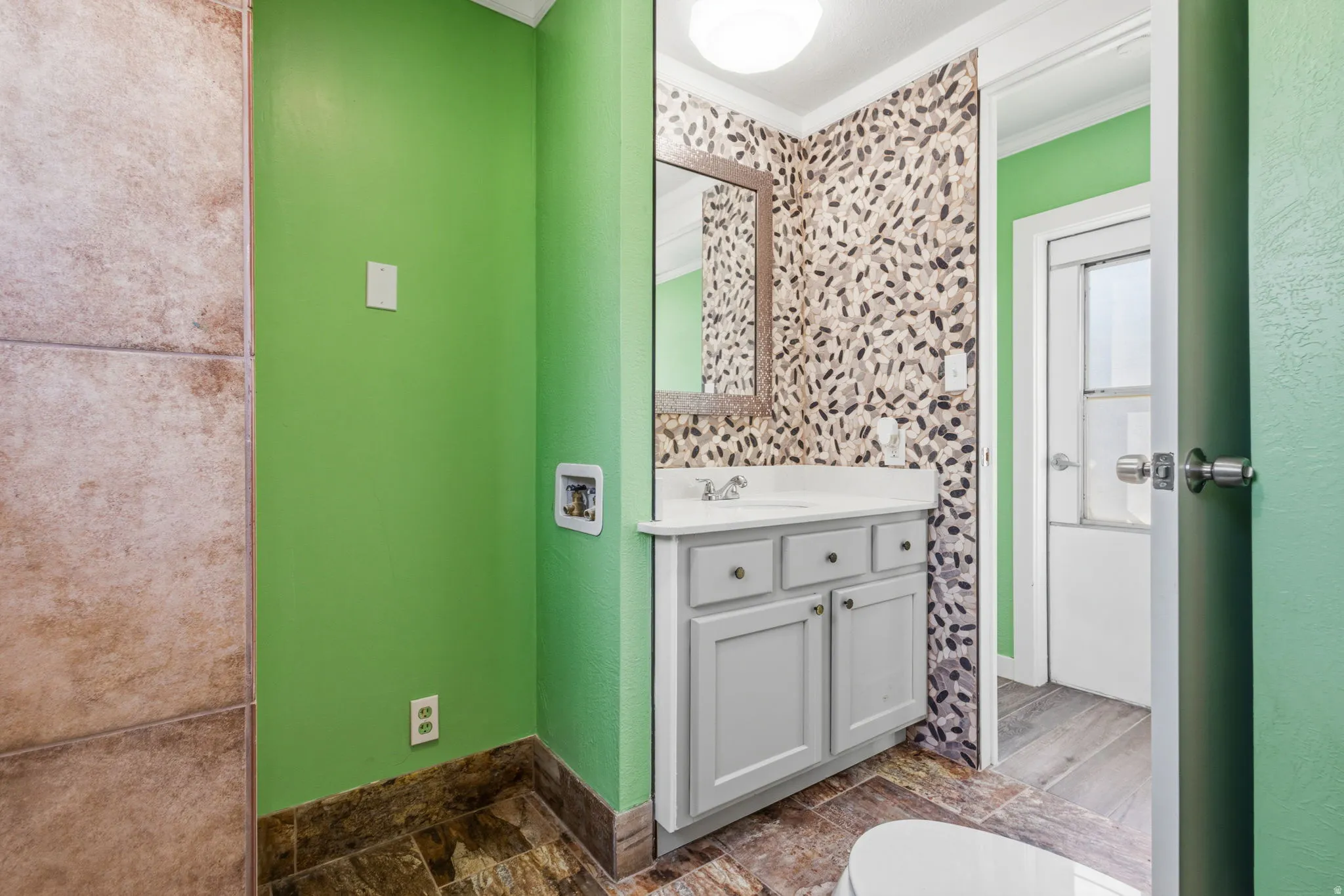 Bathroom featuring a light gray vanity with a white countertop and undermount sink, framed mirror, and patterned wallpaper