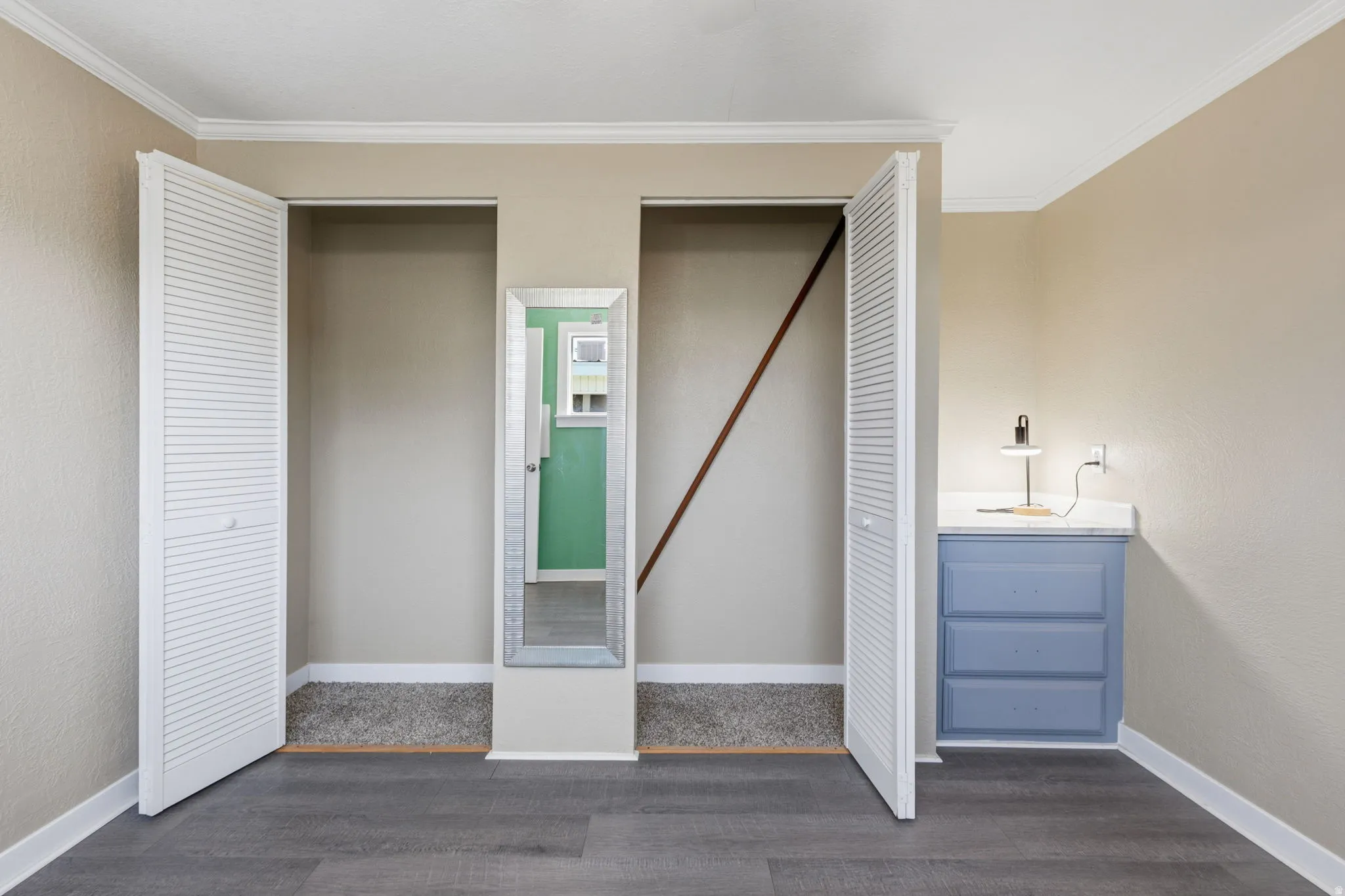 Room featuring wood-finish flooring, two closet alcoves with louvered bifold doors, and crown molding
