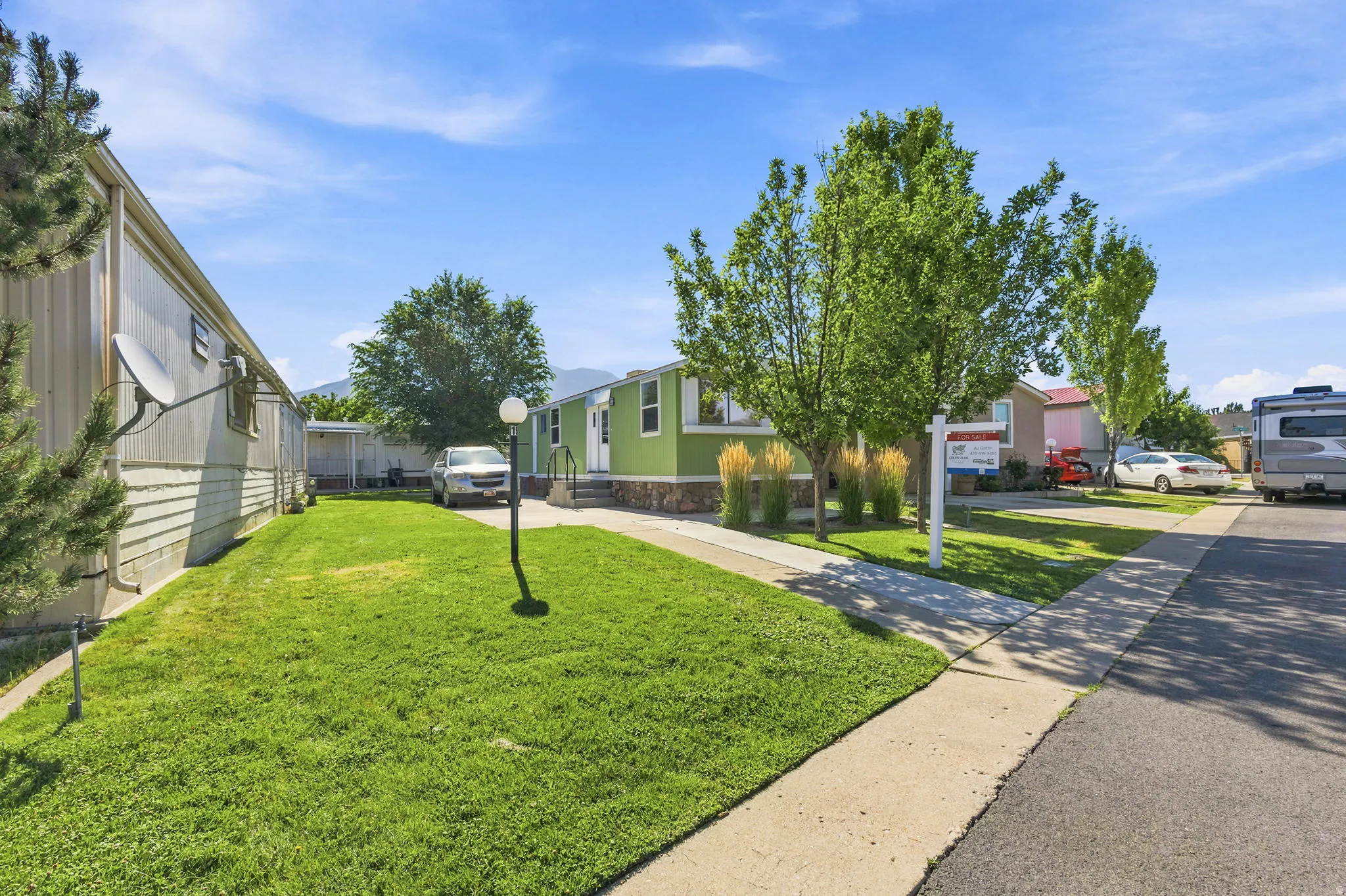 Green siding exterior with white trim, a concrete driveway, and a front lawn with mature trees and ornamental grasses