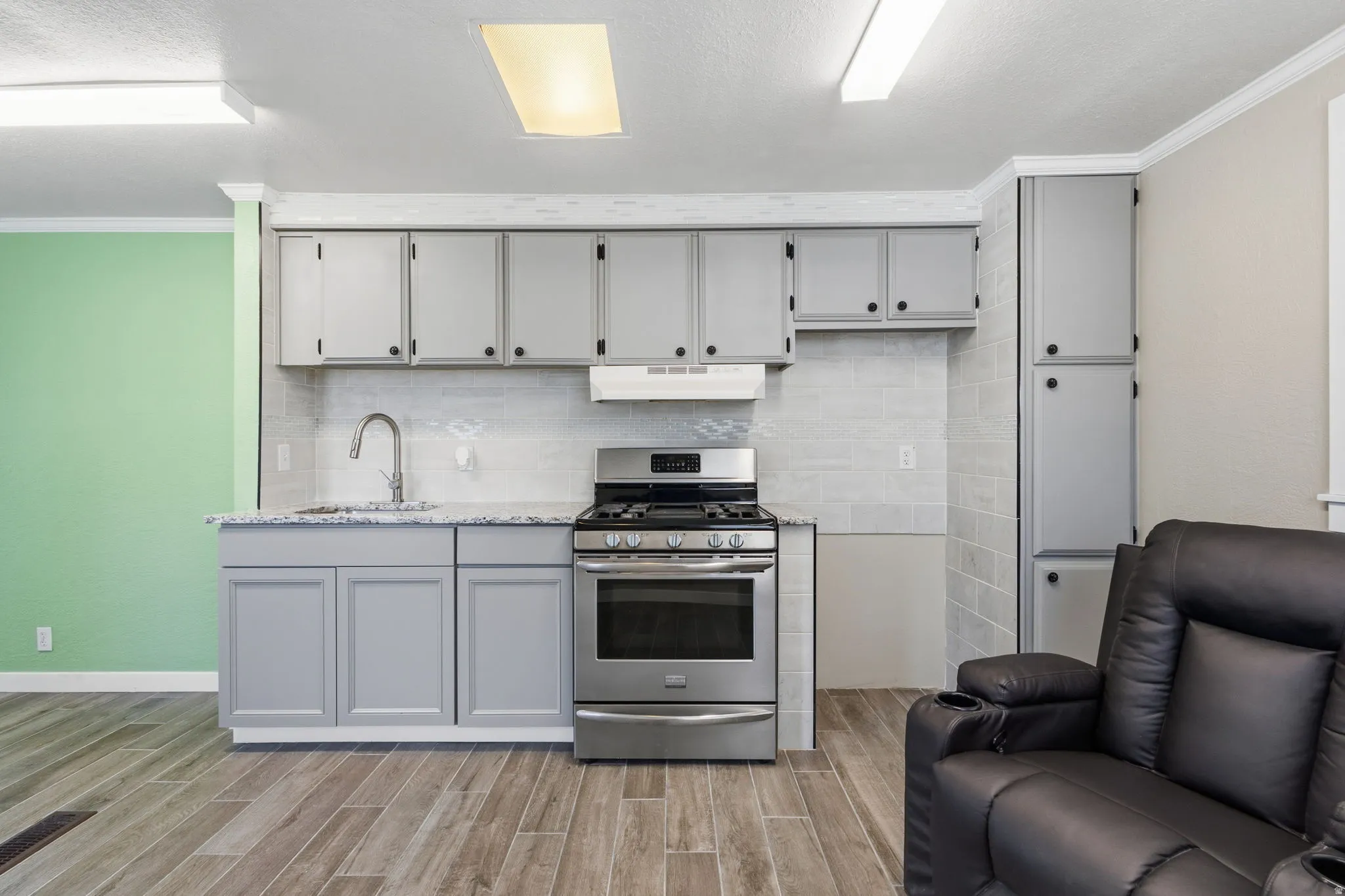 Kitchen area featuring light gray cabinetry, stainless steel range, and a light-toned tile backsplash