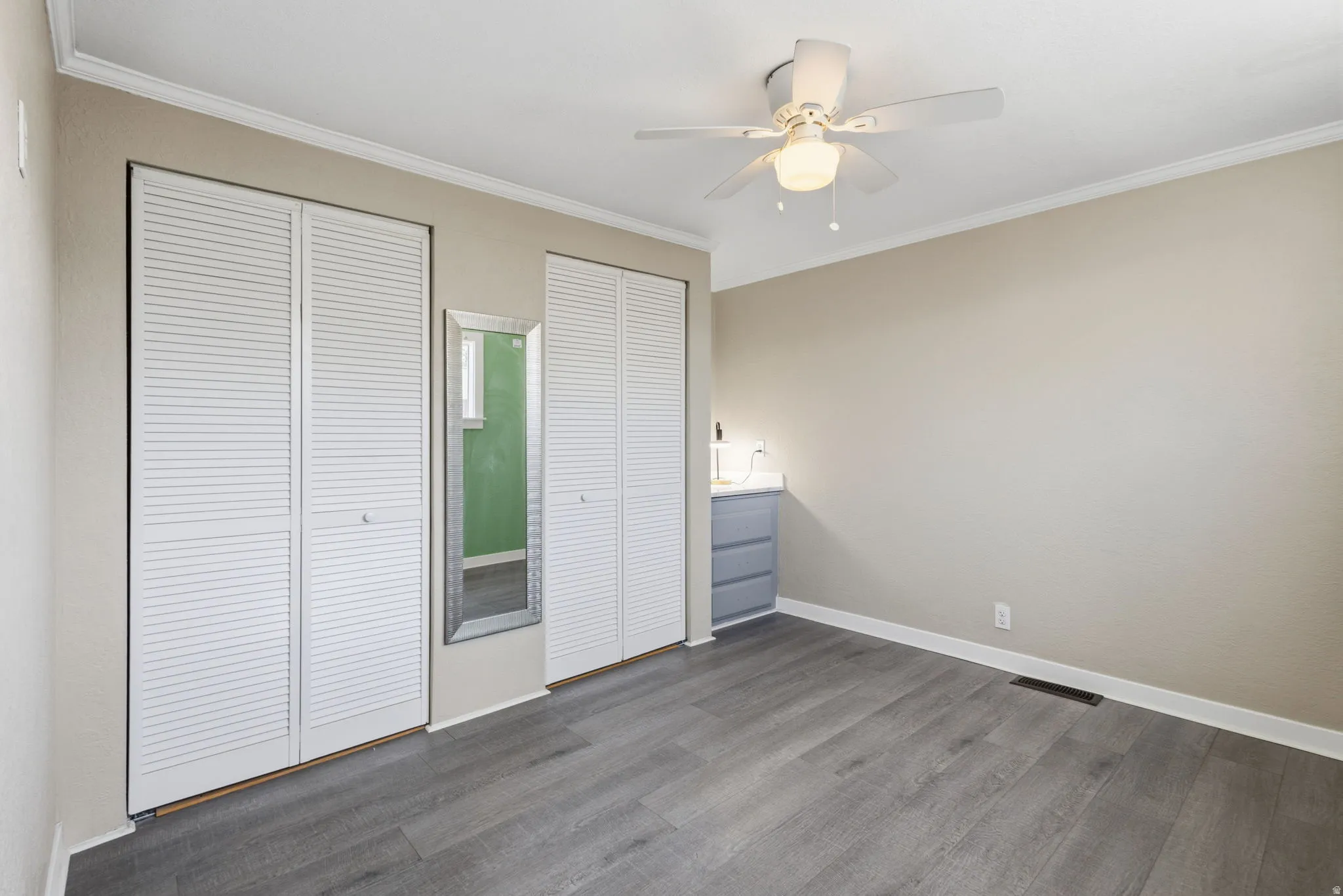 Room with wood-finish flooring, neutral wall paint, white crown molding, and white baseboards