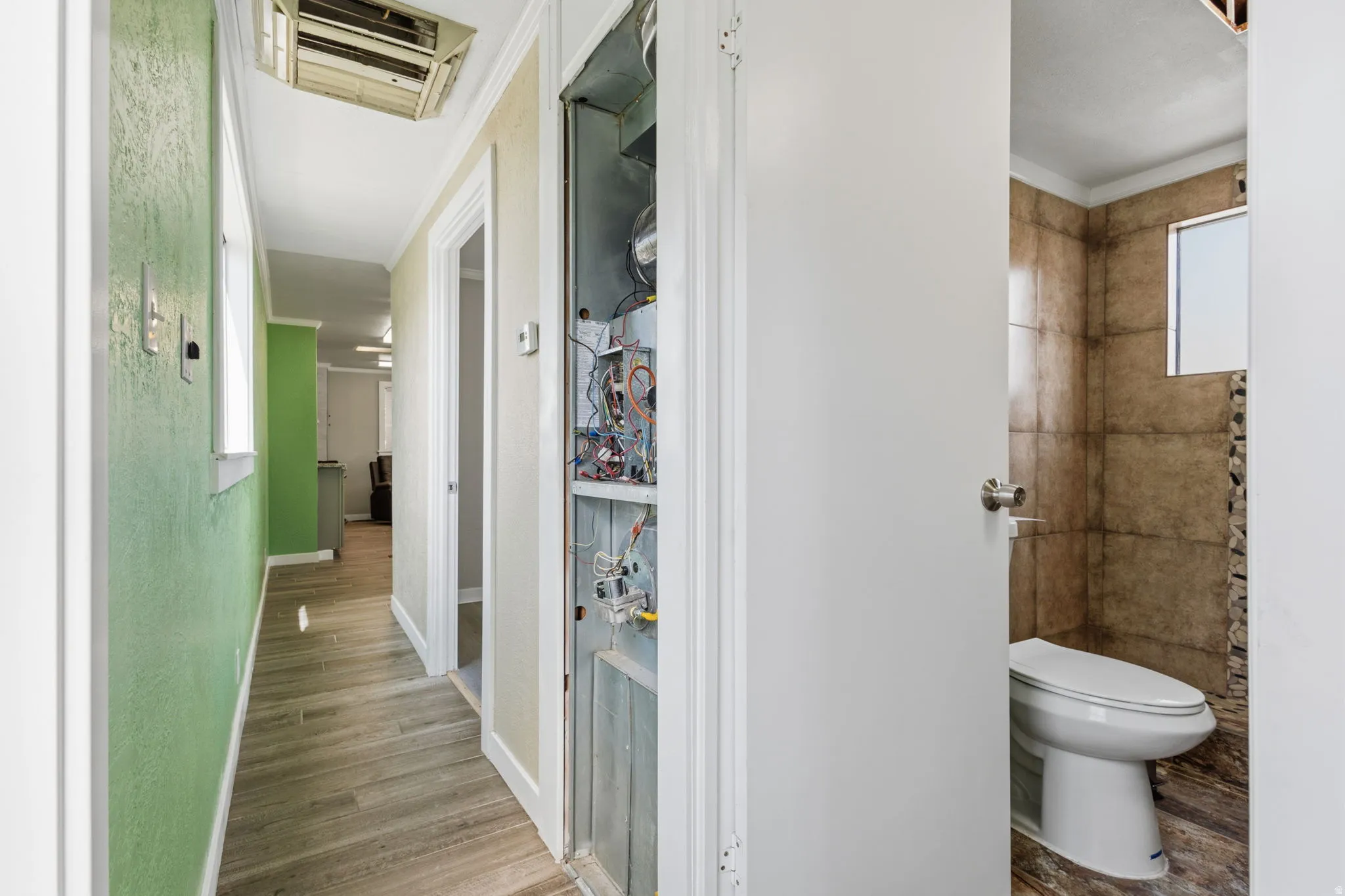 Hallway featuring wood-finish flooring, light green textured wall, and white trim
