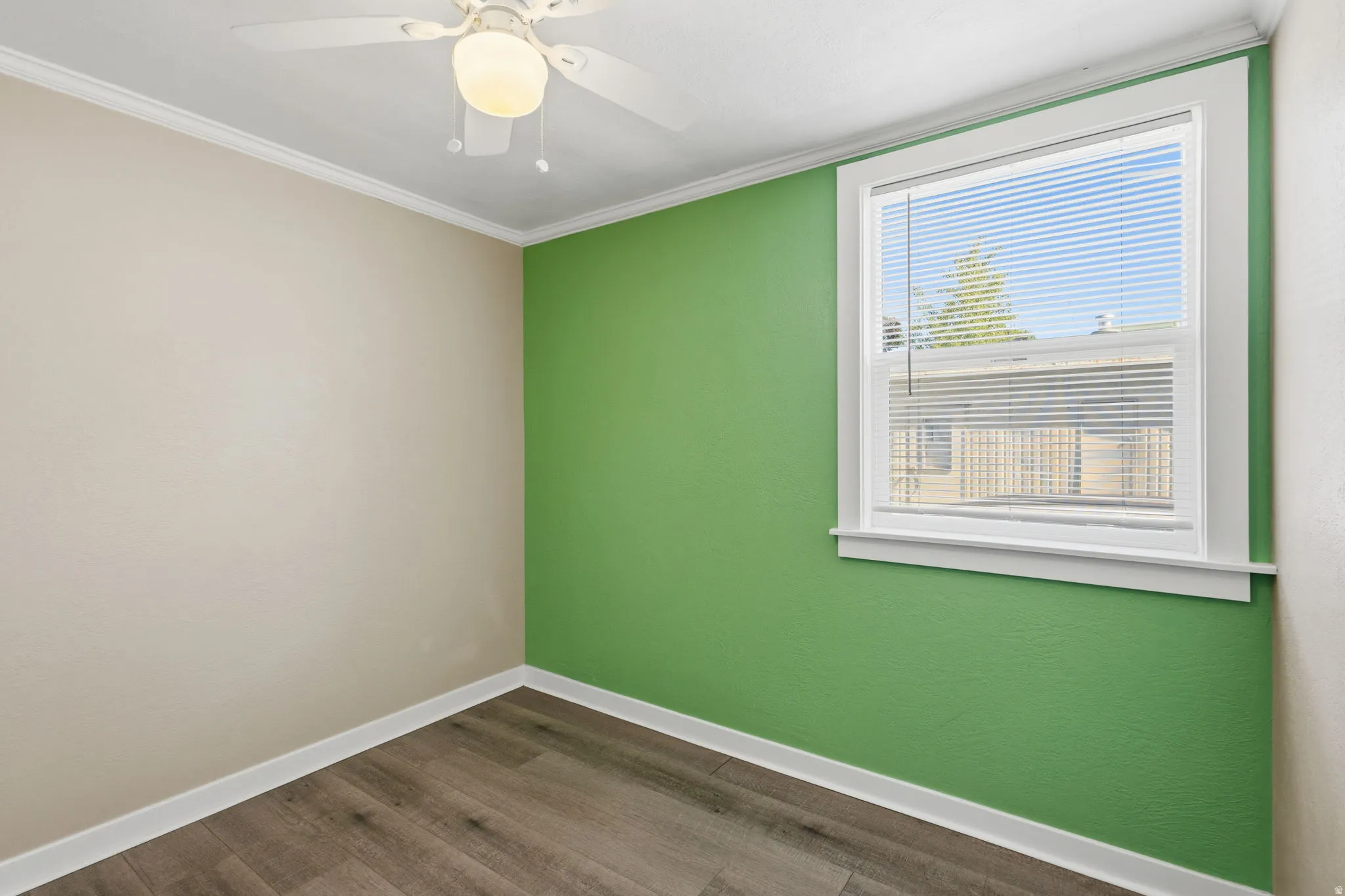 Room featuring wood-finish flooring, a ceiling fan with integrated lighting, a single window with white blinds, white trim, and two-tone wall paint