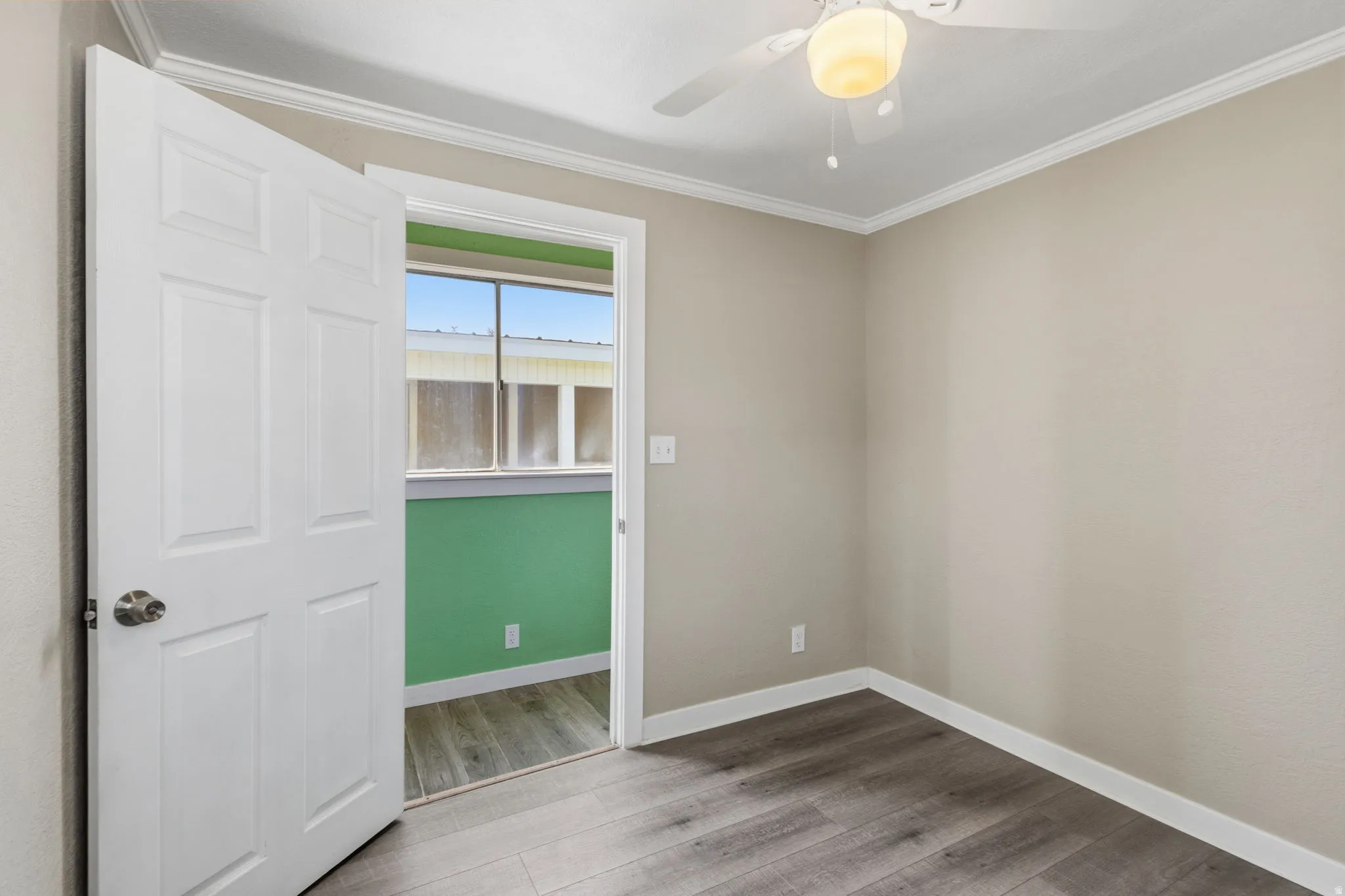 Neutral-toned room featuring wood-finish flooring, white baseboards, and a ceiling fan with integrated lighting