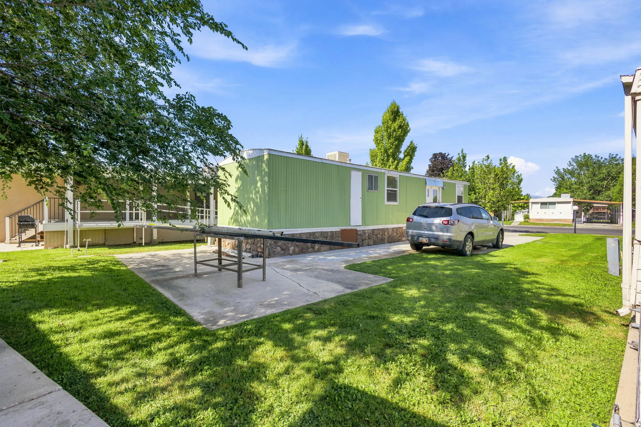 Light green exterior with stone-look skirting, featuring a concrete patio and a paved driveway