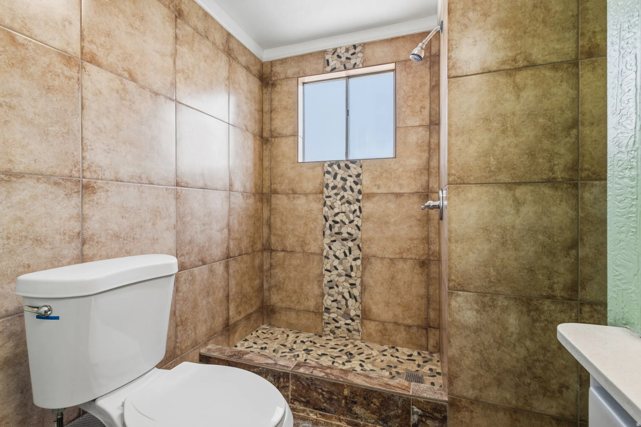 Walk-in shower with natural stone pebble flooring, integrated window, and decorative pebble tile accent