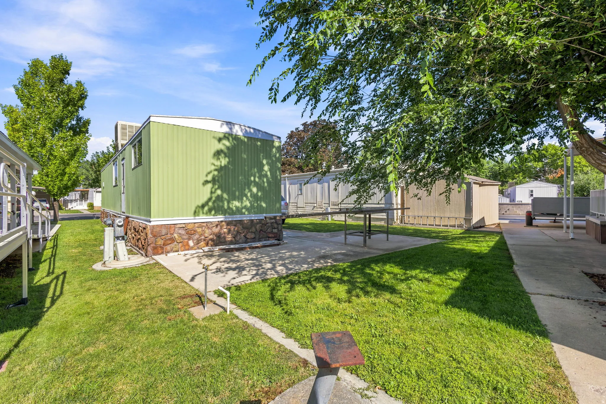 Green siding home featuring a stone-look foundation, central air conditioning unit, and a concrete patio
