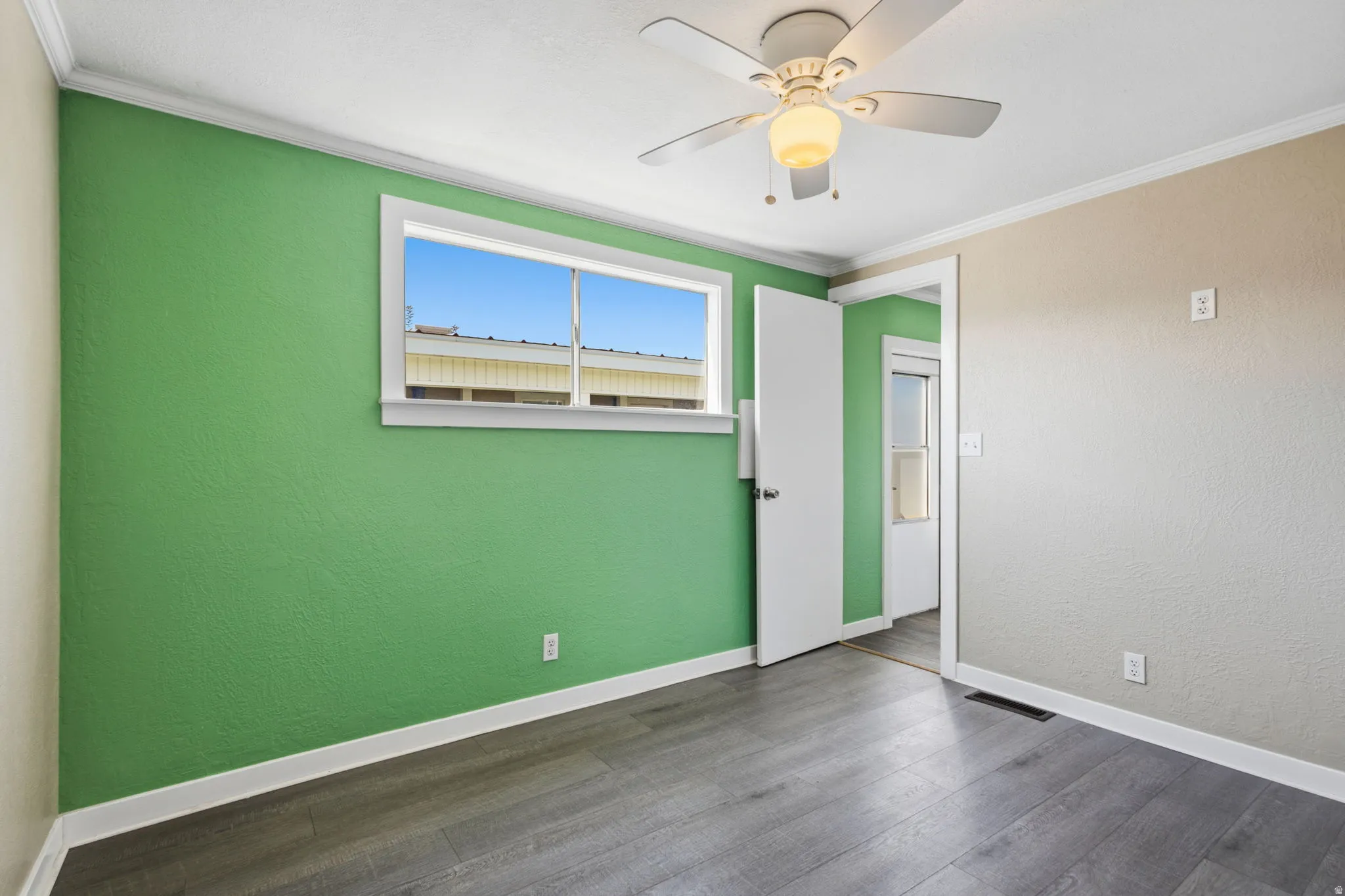Interior space featuring wood-finish flooring, a window providing natural light, a ceiling fan with light fixture, and crown molding