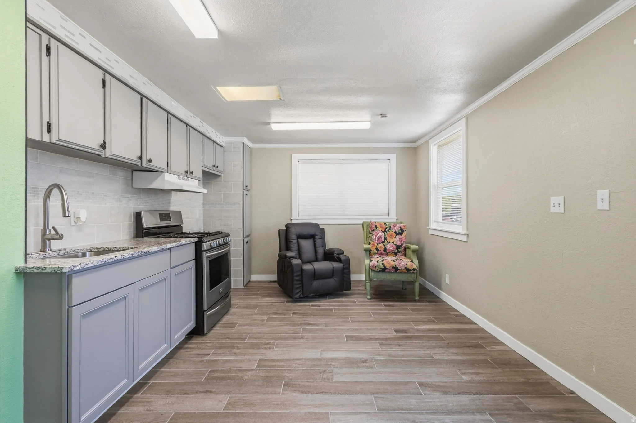 Modern kitchen featuring light gray cabinetry, granite-finish countertops, stainless-steel appliances, and a subway tile backsplash