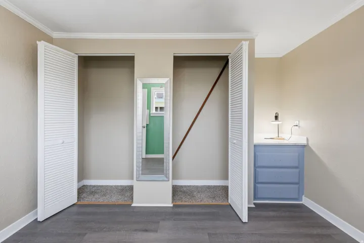 Room featuring wood-finish flooring, two closet alcoves with louvered bifold doors, and crown molding