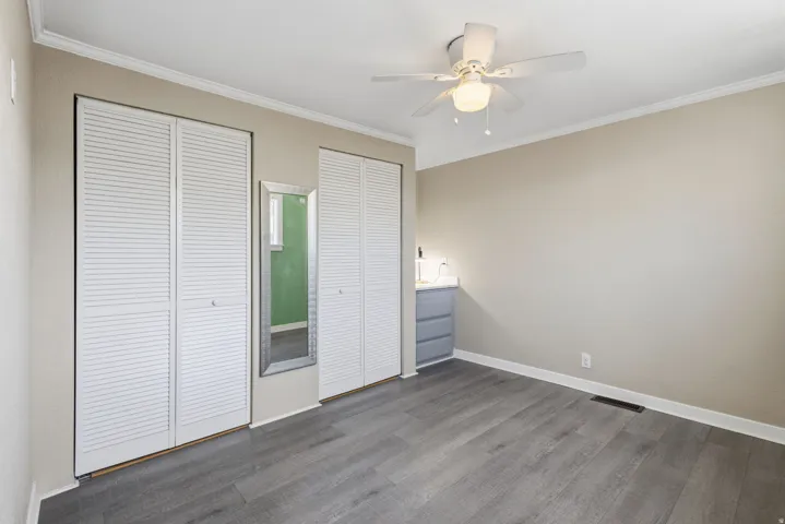 Room with wood-finish flooring, neutral wall paint, white crown molding, and white baseboards