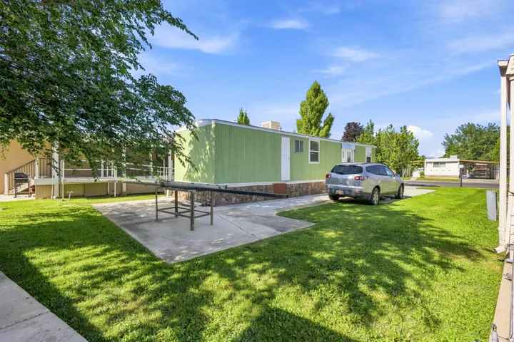 Light green exterior with stone-look skirting, featuring a concrete patio and a paved driveway