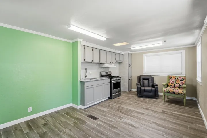 Open-concept room featuring wood-finish flooring, a kitchen area with gray cabinetry and stainless steel range, and light green accent walls