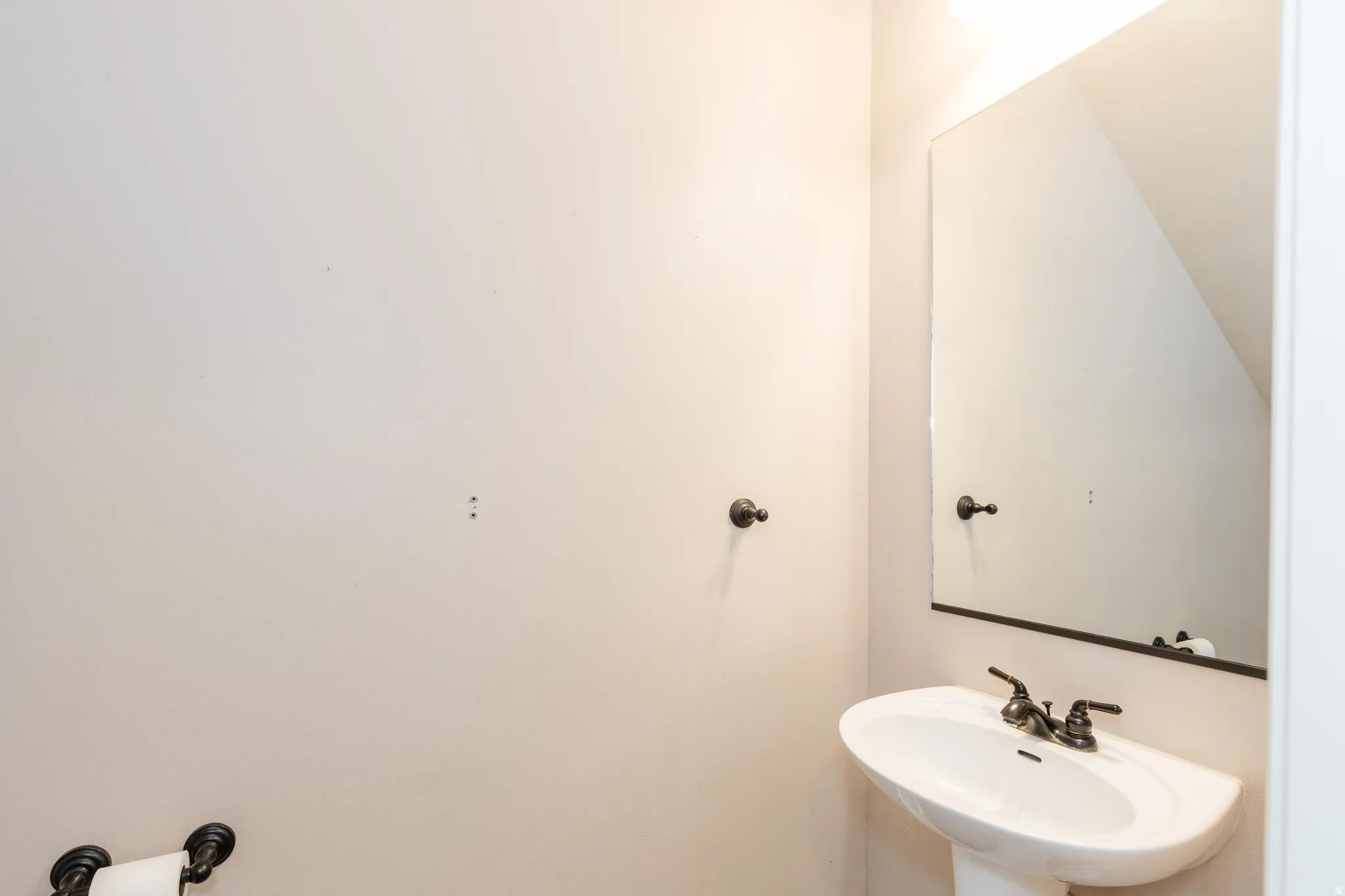 Pedestal sink with dark bronze fixtures, framed mirror, and wall-mounted towel hook
