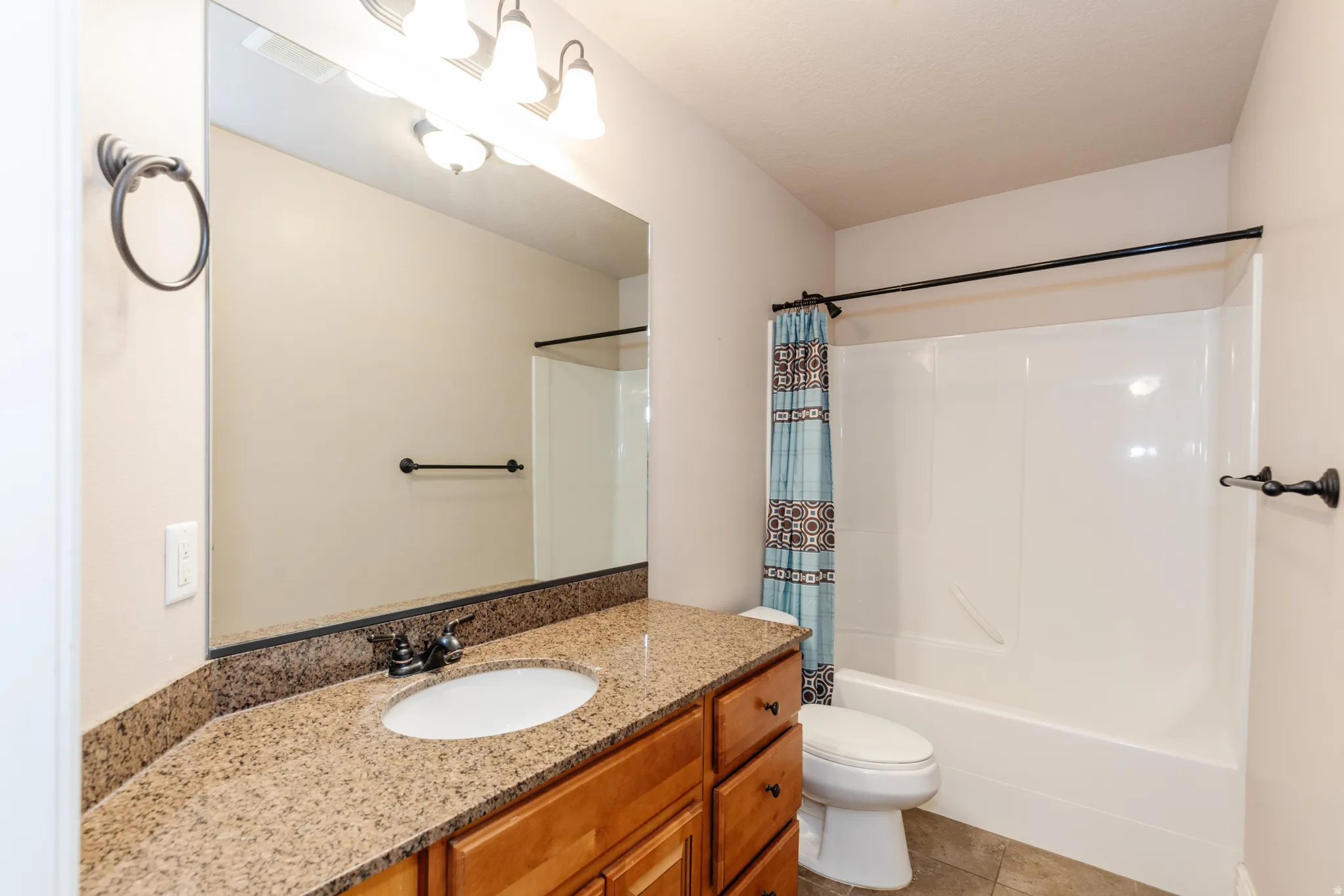 Bathroom featuring a spacious vanity with a granite countertop, undermount sink, and wood-finish cabinetry