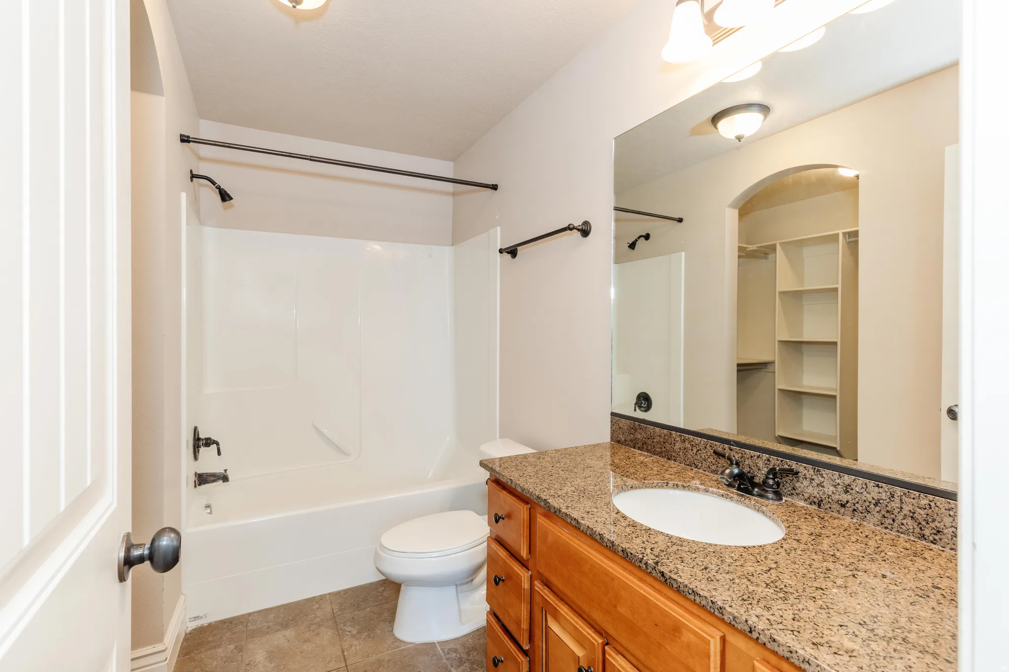 Bathroom featuring a single vanity with a granite-style countertop, undermount sink, wood-finish cabinetry, and a shower-over-tub combination with dark bronze-finish fixtures