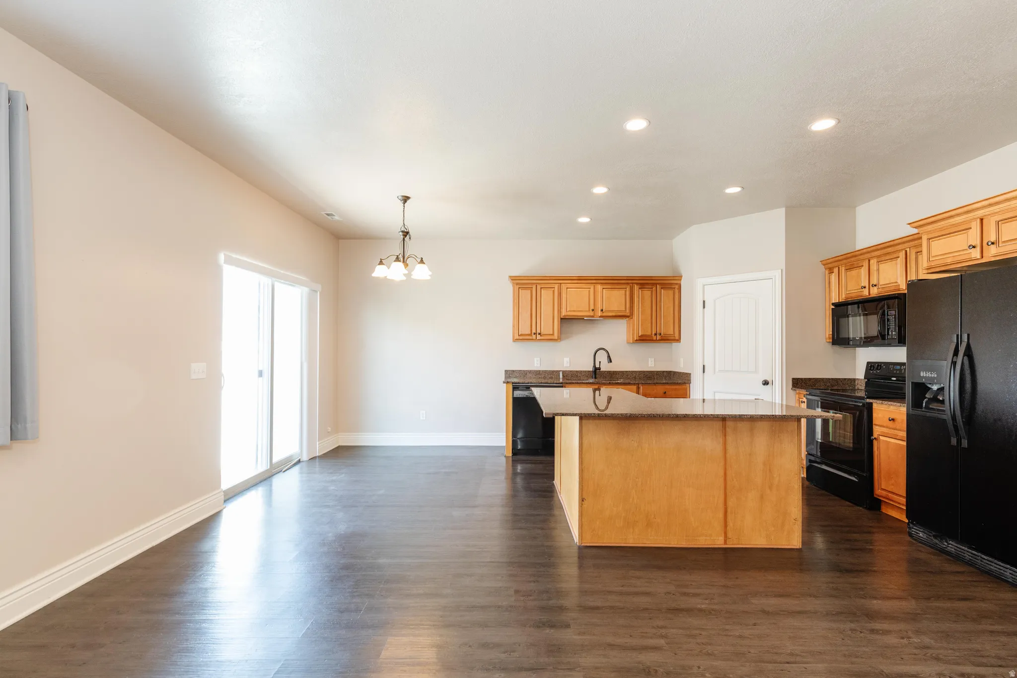 Open-concept kitchen and dining area featuring rich wood-finish flooring, light wood cabinetry, and dark countertops