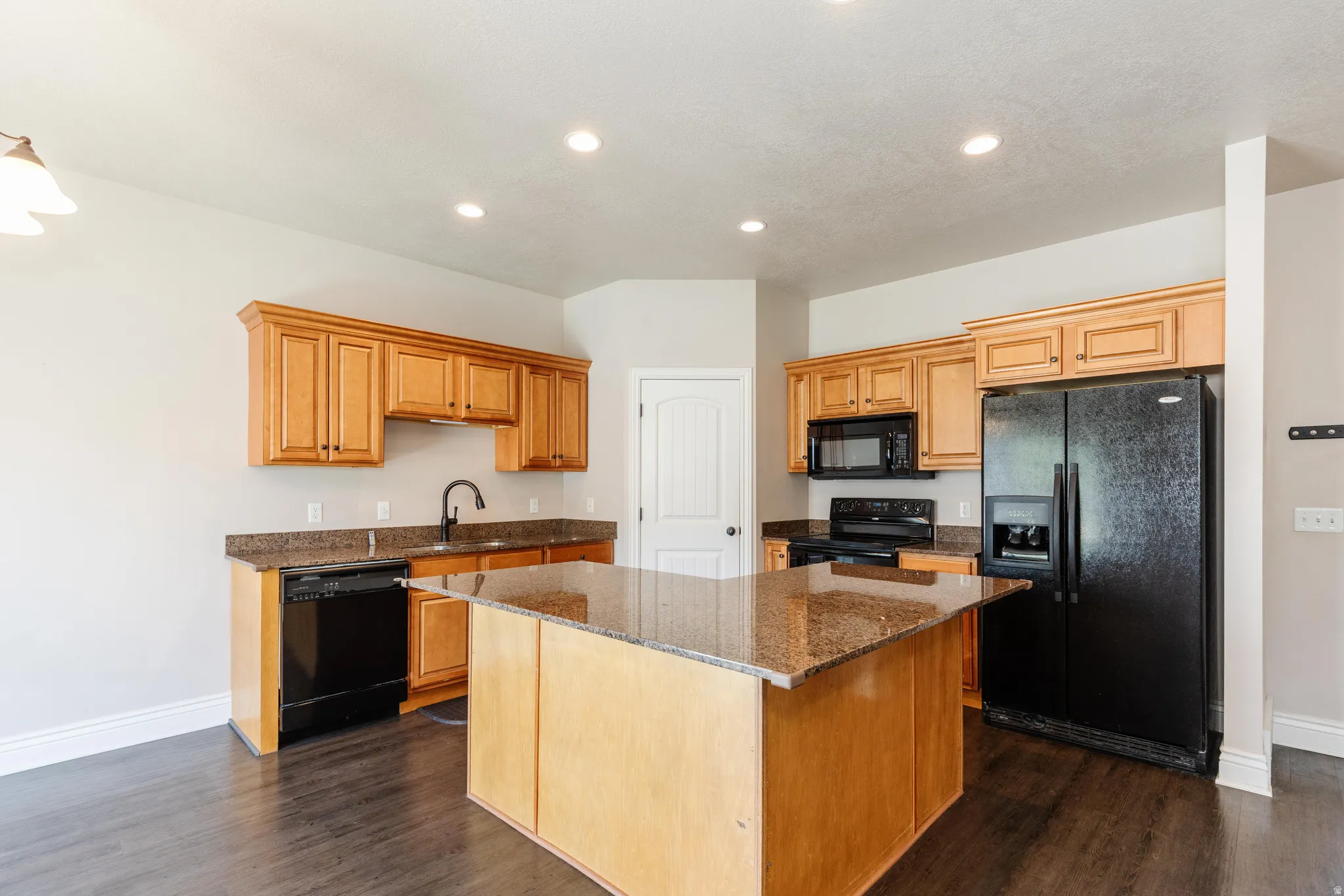 Kitchen featuring a central island with a stone-finish countertop, wood cabinetry, dark-finish appliances, recessed lighting, and wood-finish flooring