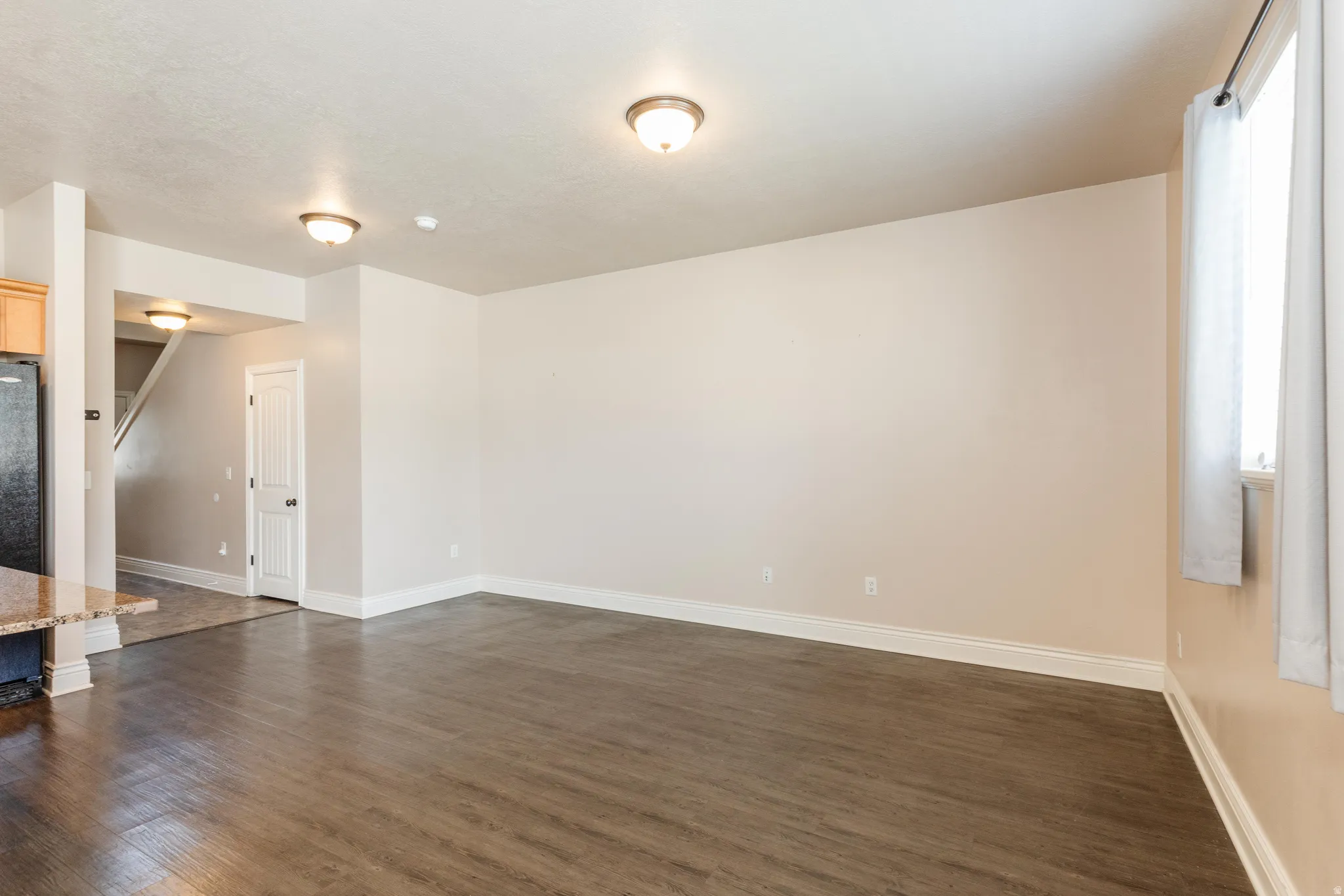 Spacious living area featuring wood-finish flooring, white baseboards, and neutral wall paint