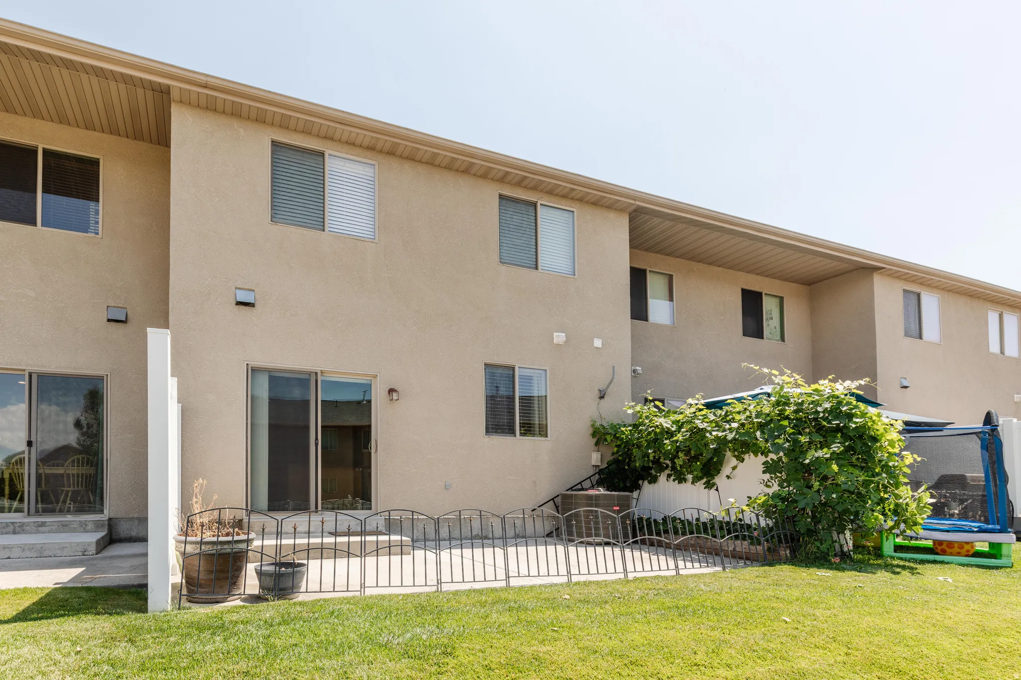 Expansive grassy backyard featuring two sliding glass doors, multiple windows, and an outdoor patio space